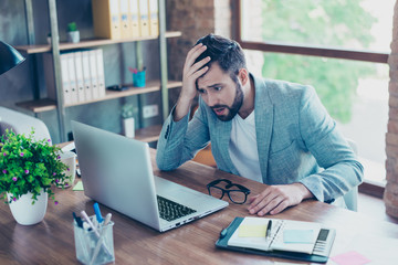 Oh no! Portrait of attractive businessman holding hand on head, looking very disappointed, looking at screen of computer, having mouth opened and disbelieve emotion on his face