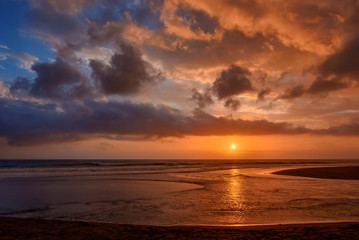Dramatic sunset clouds reflected on the water sea. Tropical beach landscape at golden hour