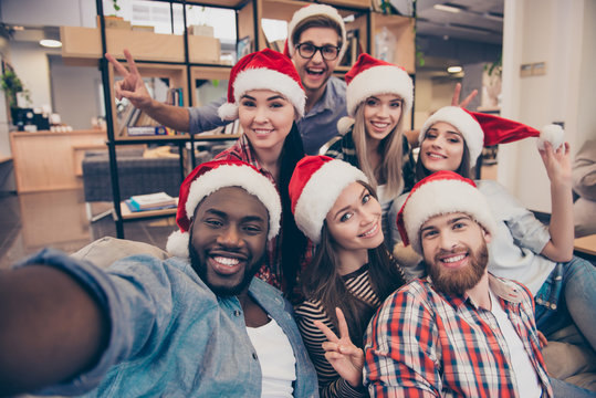 Self portrait of mixed race friends : african, american, asian, caucasian,  young smiling bearded men and beautiful women in red christmas hat showing peace symbol  to the camera