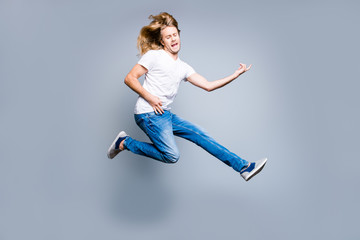 Music is my life! Excited and amazed young guy with blonde long hair in casual clothes is celebrating his victory, he is playing an imaginary guitar, isolated on grey background