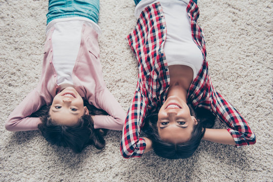 Top view photo of happy mother and sweet daughter wearing casual clothes, they are lying comfortably on the floor with crossed hands behind their heads
