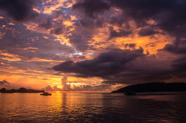 Obraz premium A fiery sun is setting in the bay of Kota Kinabalu, Borneo, colorizing the cloudy sky in a dramatic fashion