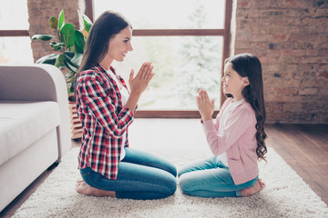 Happy cheerful mother and preteen daughter in casual clothes are sitting on the carpet, playing a game and holding their hands together
