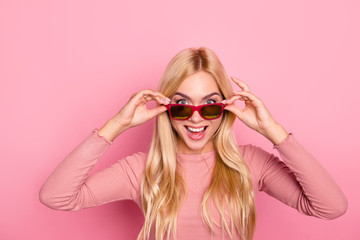 Attractive young amazed cool girl with long blonde hair is touching her glasses. Isolated on bright pink background