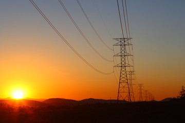 Fototapeta premium High-power electric distribution tower with the setting sun in the background