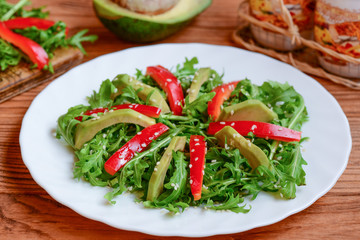 Avocado, arugula and red pepper salad on a white plate. Homemade arugula and avocado salad with red pepper and sesame seeds. Raw food diet. Veganism. Closeup