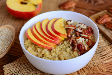 Breakfast quinoa porridge with apples and nuts topping. Vegetarian quinoa porridge with apples and pecan nuts in a white bowl. Rustic style. Closeup