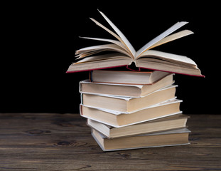 Pile of books and an open book on a wood table and a black background