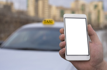 Close-up of a hand of a man holding a mobile phone in the background of a car and a city, booking a taxi. Mock up a clean smartphone screen for the design of your advertisement.