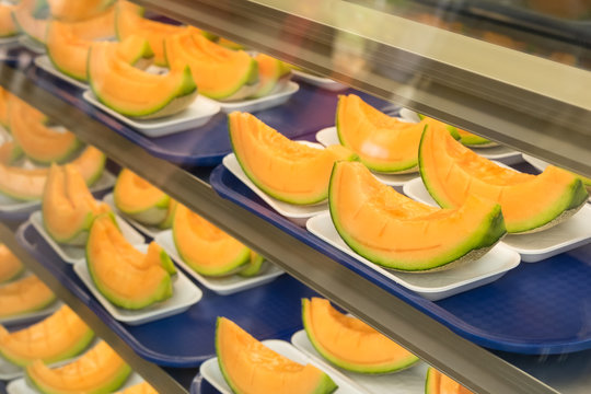 Bright yellow sweet melon sliced into pieces for sell in a glass show fridge. Reflection on the glass of refrigerator. 