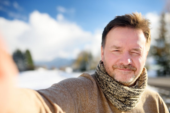 Handsome milddle age man making a self portrait (selfie) with snowy Bavarian Alps on background