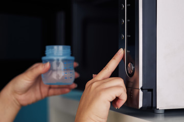 Close up of female hands putting a baby bottle with water into a microwave