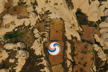 Top view of land and big hot air balloon. Landscape of goreme, cappadocia in Turkey. The balloon is flying high and go with the wind. The land is full of hills and valleys. twirling pattern on balloon