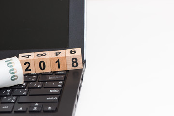 The wooden cube for new year 2018 on laptop with banknote