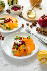 Plates of Belfian waffles with persimmon, pomegranate seeds and sour cream on white table cloth