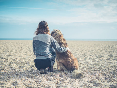 Young woman sitting on beach with big dog