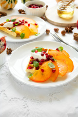 Plates of Belfian waffles with persimmon, pomegranate seeds and sour cream on white table cloth