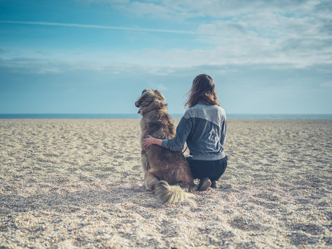 Young woman sitting on beach with big dog