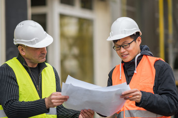 Young Asian intern at work on construction site with senior engineer. Outdoors
