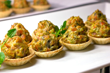 Tartlets with baked vegetables and herbs on a white porcelain dish