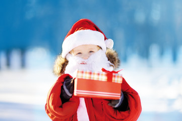 Funny little boy wearing Santa Claus costume in winter snowy park