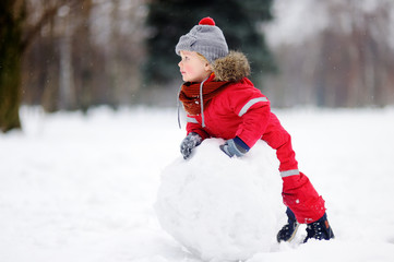 Fototapeta na wymiar Little boy in red winter clothes having fun with snowman