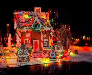 Adorable gingerbread family near big snow-covered homemade gingerbread house with Christmas lights