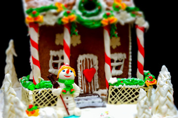 Close up of bright sugar snowman near big snow-covered homemade gingerbread house