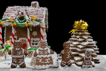 Cute gingerbread family near snow-covered homemade gingerbread house and Christmas tree