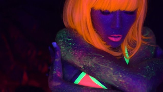 Sexy woman with fluorescent make up face and body in orange wig, creative makeup look great for nightclubs. Halloween party, shows and music concept - slow motion video