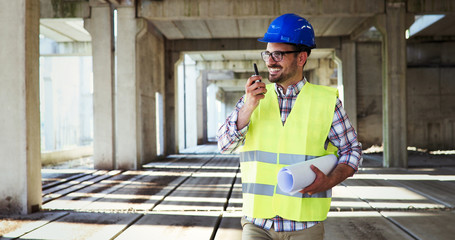 Male architect with blueprints using walkie-talkie