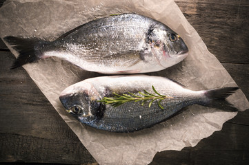 Fresh fish dorado on the parchment paper with thyme on the wooden table. Top view with copy space