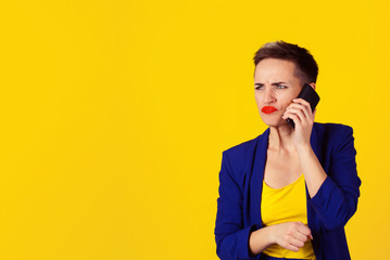 Closeup portrait angry young woman, teenager talking on cell phone, having unpleasant, bad conversation isolated yellow wall background. Negative human emotions, facial expressions, reaction, feelings