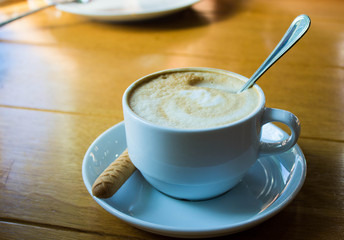 White cup of coffee on wooden table background, front view. Cappuccino latte in cafeteria.