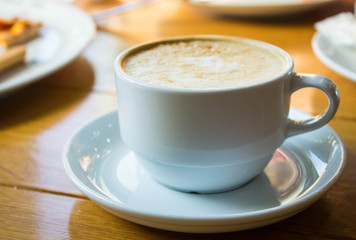 White cup of coffee on wooden table background, front view. Cappuccino latte in cafeteria.