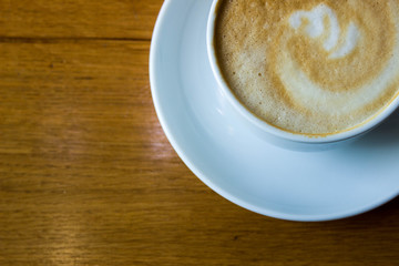 White cup of coffee on wooden table background, top view. Cappuccino latte in cafeteria.