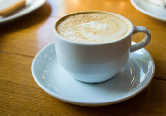 White cup of coffee on wooden table background, front view. Cappuccino latte in cafeteria.