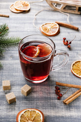 Hot berry tea with a lemon. Red herbal tea in glass cup on wooden grey table. Green fir-tree branch, dried orange, cinnamon