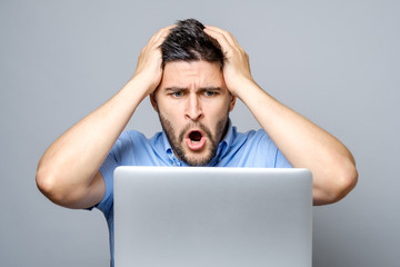 Young shocked man in blue shirt using laptop