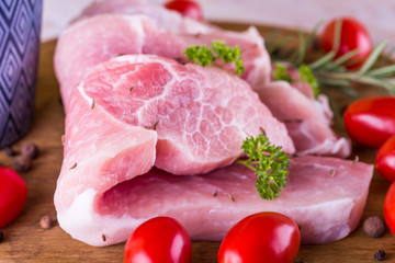 Few long slices of pork meat on wooden board with red tomatoes