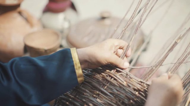 An adult man in a national costume is weaving a basket. An old Muslim is weaving a basket of twigs. National holiday in the east. A man in a mountain.