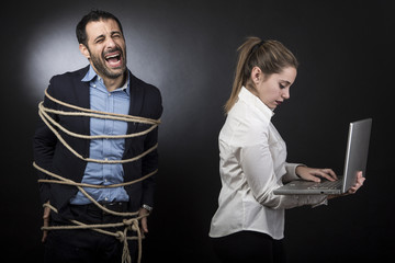 un uomo disperato in giacca è legato mentre la sua compagna controlla il suo computer - sfondo scuro 