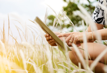 Hands using tablet computer in green field