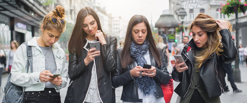 Group of four girl friends with smartphones on the street