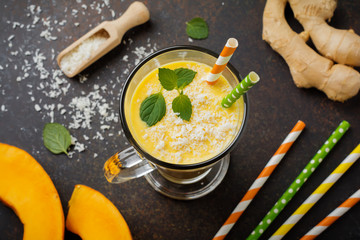 Pumpkin smoothies with ginger and coconut shavings and mint in a glass on a dark stone or concrete background. Healthy and delicious drink for breakfast. Selective focus. Top view. Copy space.
