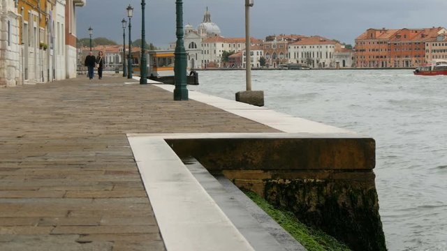 VENICE, ITALY, SEPTEMBER 7, 2017: A beautiful view of the Venice embankment on the Gande Canal, the waters of which are beating against the shore, along which people are strolling