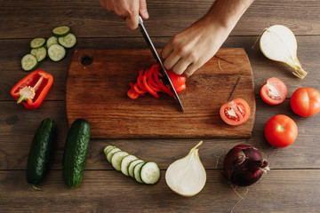 The chef cuts fresh and tasty vegetables for cooking. Hands close-up. View from above. Wooden brown background. Beautiful food still life.