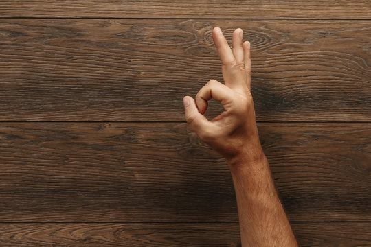 A Man's Hand Shows Ok On A Wooden Brown Background. Copy Space.