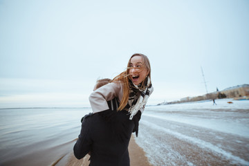 Winter love emotions of joyful couple enjoying time together outdoor at city beach. Lovely true moments, man holding and lifting up his happy woman