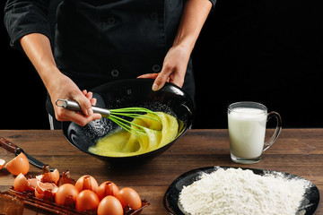 Whipping eggs. Chef hands close-up whisk eggs on a black background. Natural light, slightly toned image. Copy space.